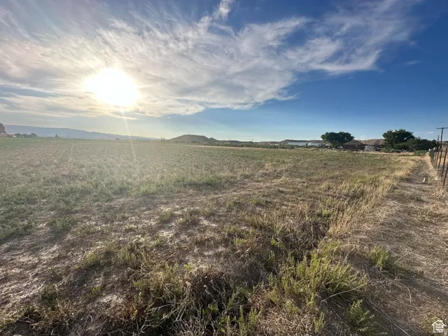 Expansive open parcel featuring natural ground cover, a partial wire fence line, and distant residential structures under a broad sky