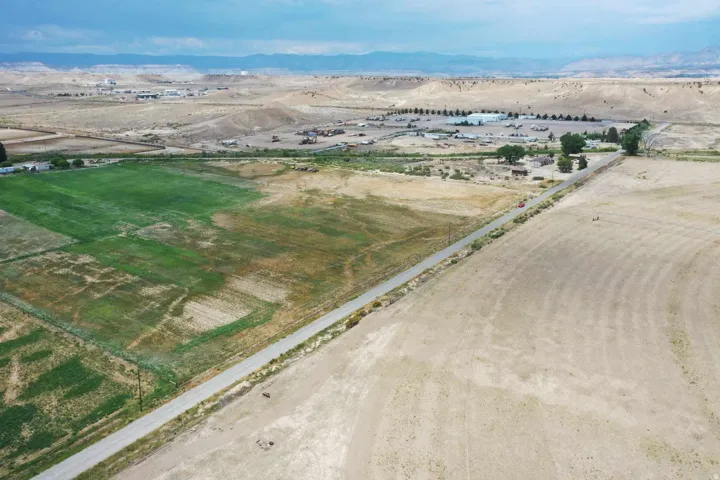 Expansive agricultural land featuring a paved road, varying terrain, and distant hills