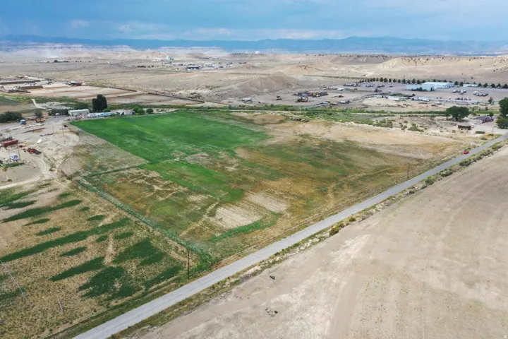 Expansive undeveloped land featuring a paved road frontage, defined property boundaries, and distant mountain backdrops