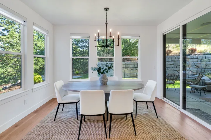 Bright dining area featuring hardwood-finish flooring, multiple windows, a sliding glass door, and a black wrought-iron chandelier
