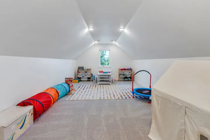Bright attic space featuring sloped ceilings, recessed lighting, and a window for natural illumination