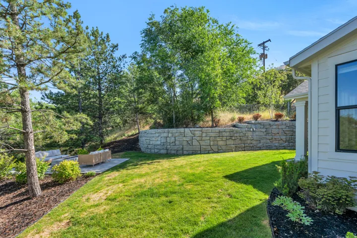 Expansive lawn with a stone retaining wall, mature trees, and a paved patio area
