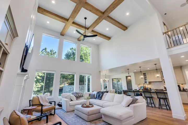 Two-story living area featuring a coffered ceiling with wood beams, a contemporary ceiling fan, recessed lighting, and a wall of windows