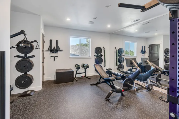 Dedicated fitness space featuring impact-absorbing rubber flooring, a large wall-mounted mirror, multiple windows, and recessed lighting