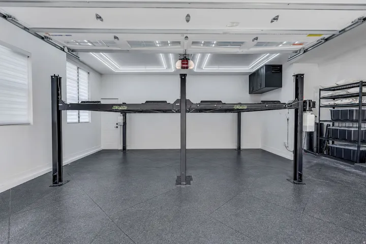 Garage space featuring a four-post vehicle lift, durable tile flooring, and integrated ceiling lighting