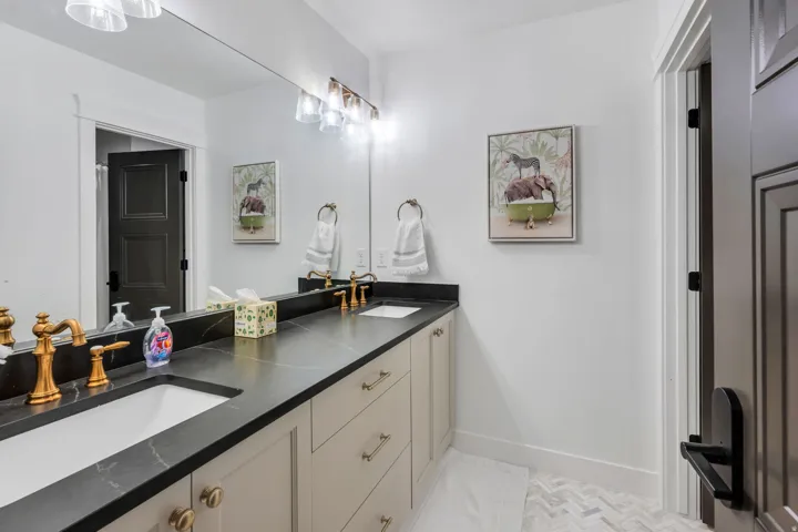 Bathroom featuring a dual vanity with undermount sinks, dark countertops, brass-finish fixtures, and herringbone tile flooring
