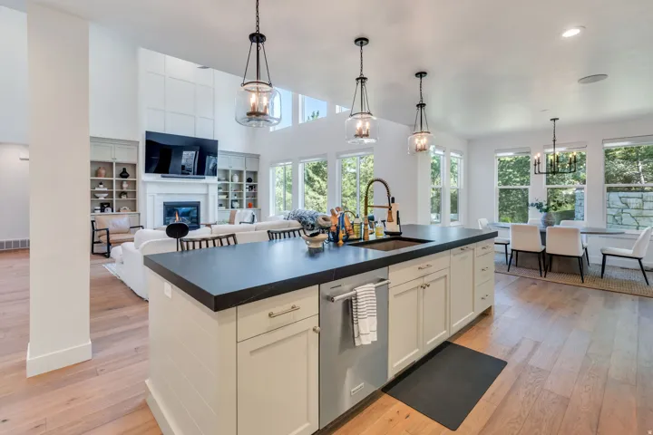 Kitchen island featuring a dark countertop, integrated sink with a gooseneck faucet, and light-toned cabinetry