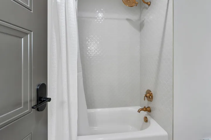 Bathtub with textured white wall tile and brass fixtures