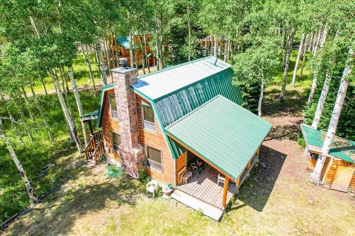 Wood-clad cabin featuring a green metal roof, stone chimney, and an attached covered porch