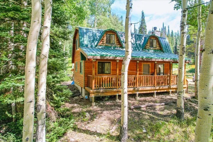 Log cabin exterior featuring a green metal roof, a covered wooden porch with railings, and two dormer windows