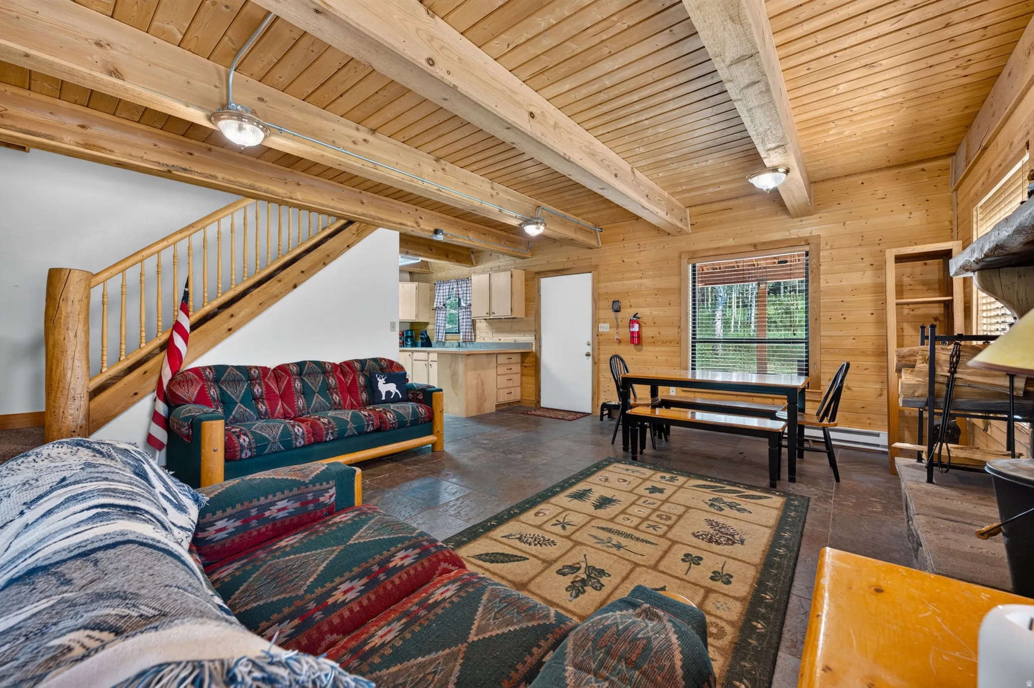 Open-concept living space featuring wood-paneled walls, exposed wood beams, and textured flooring