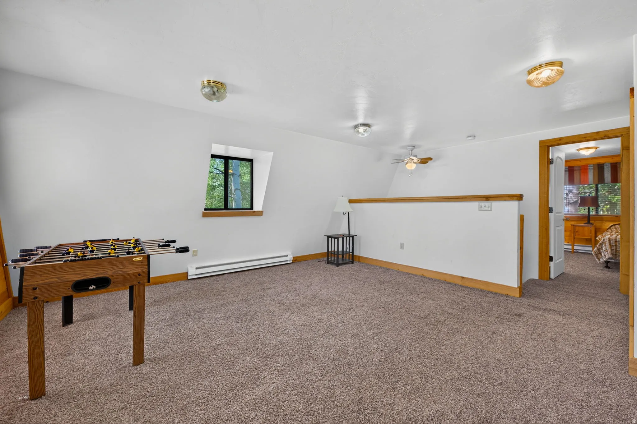Open loft area with sloped ceilings, plush carpeting, and a built-in half-wall railing featuring wood trim
