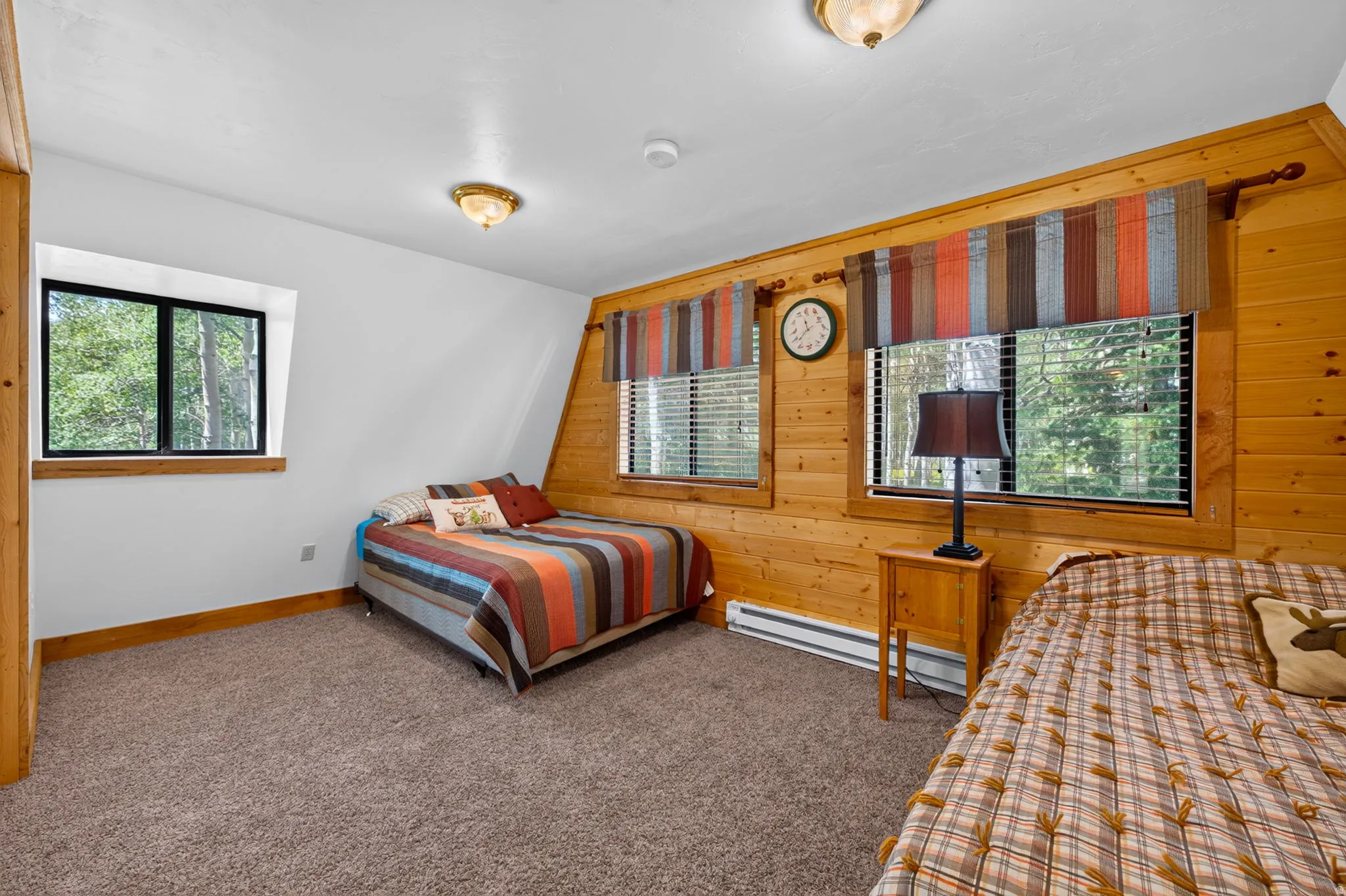 Angled ceilings with recessed lighting, wood-paneled wall, carpeting, and two windows featuring blinds