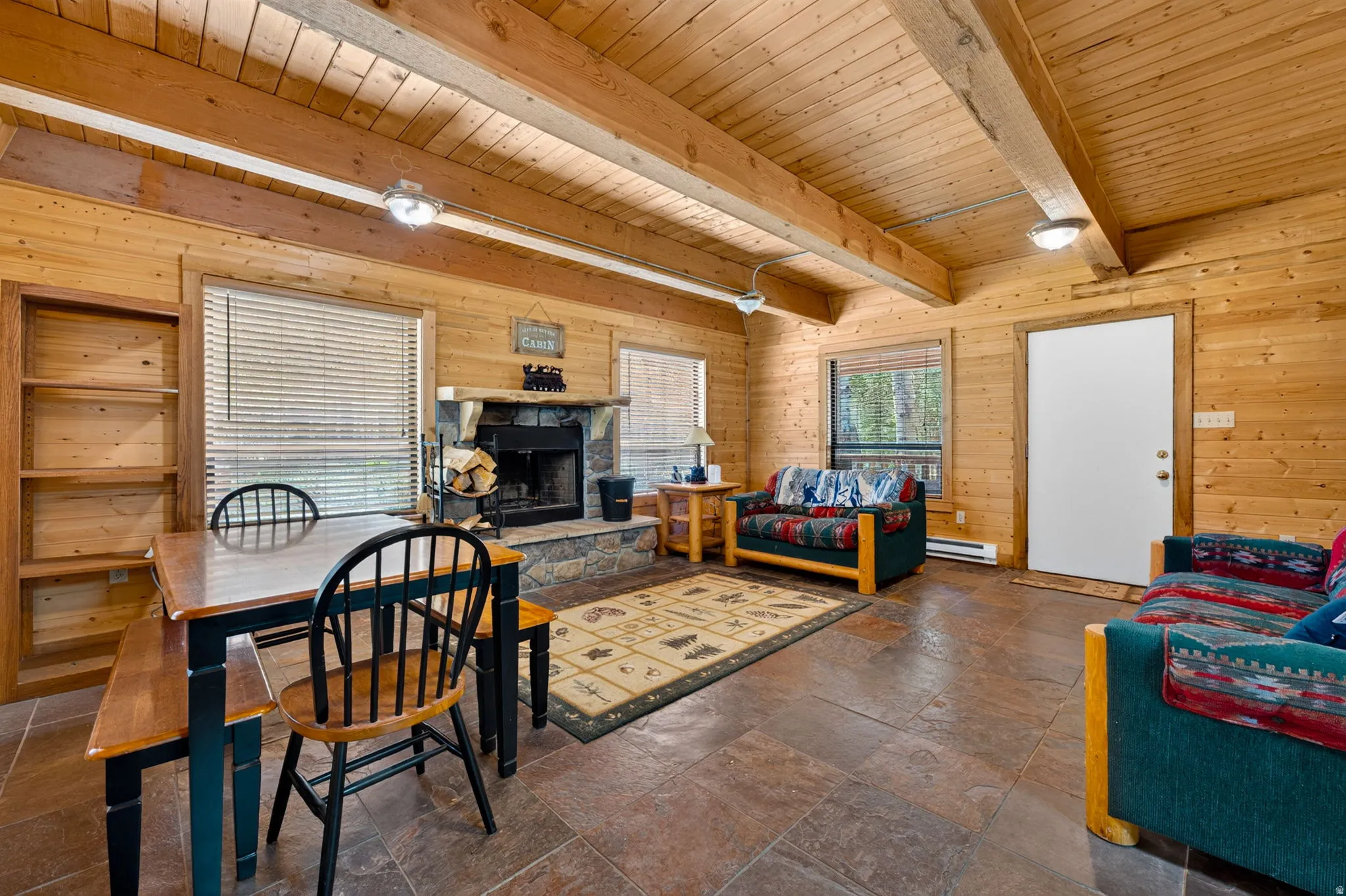 Spacious living area featuring extensive wood-paneled walls, exposed wood ceiling beams, and stone-tiled flooring
