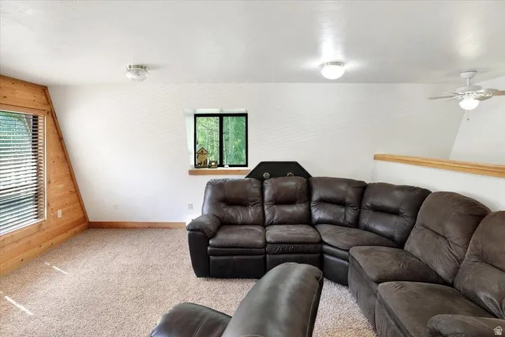 Carpeted living space featuring an angled wood-paneled wall, multiple windows, a wood railing, and a ceiling fan