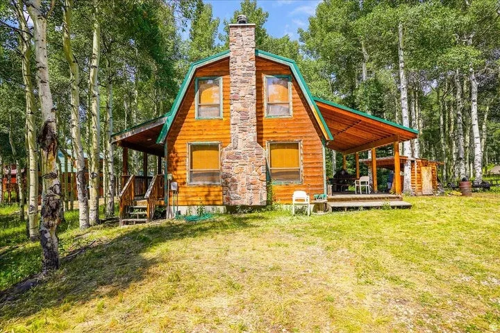 Wood-sided cabin featuring a gambrel roofline and a prominent stone chimney