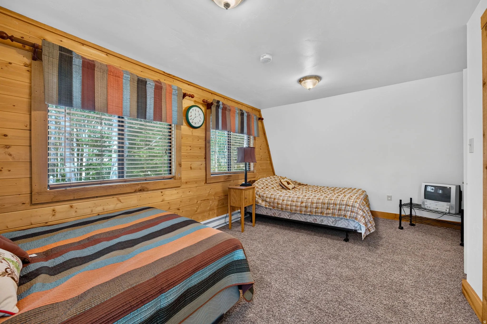 Room featuring wood-paneled walls, two windows with blinds, a white ceiling with flush-mount lighting, and wall-to-wall carpeting