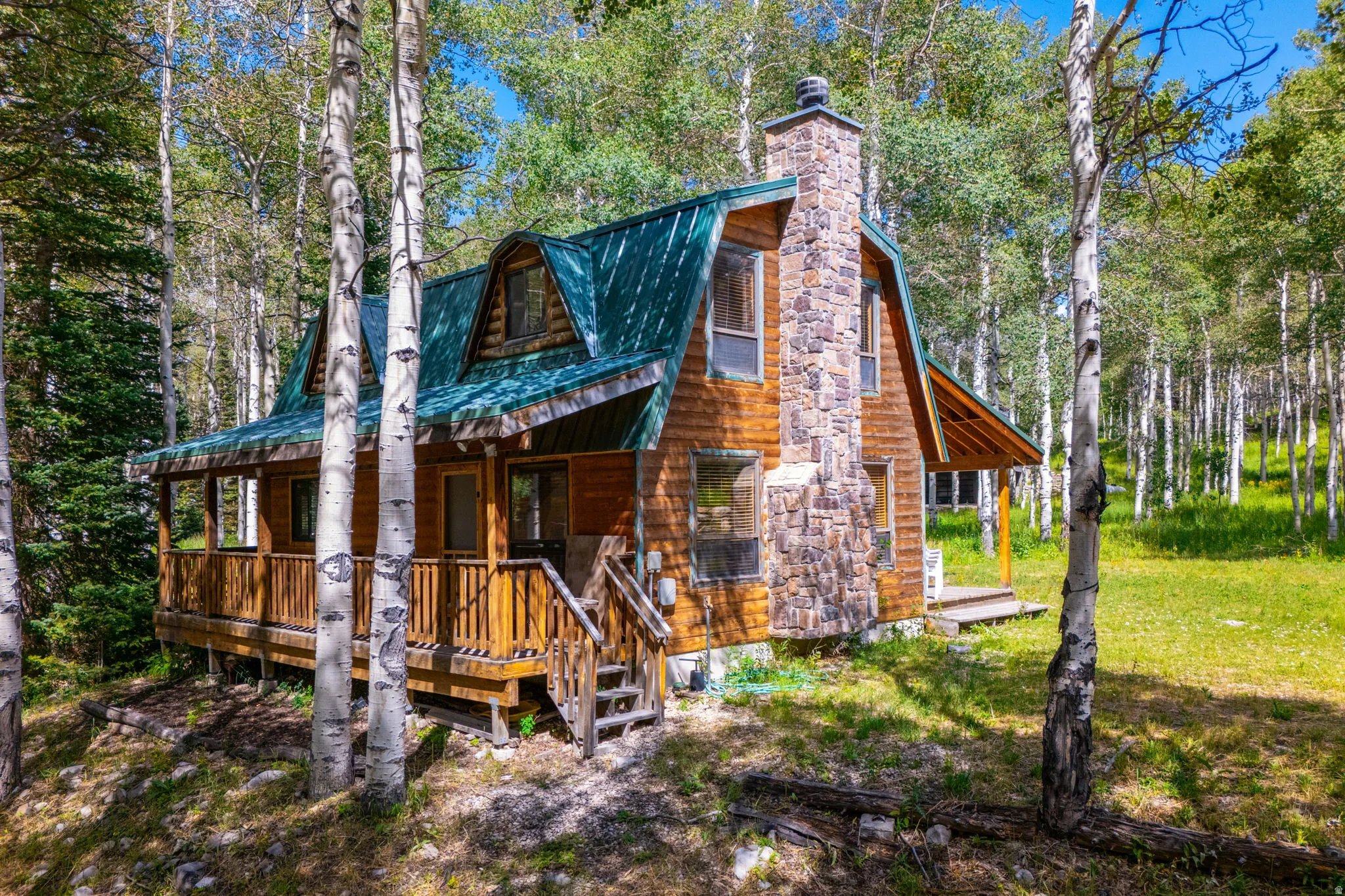 Wood-sided cabin featuring a stone chimney, covered porch, and dormer windows under a green metal roof