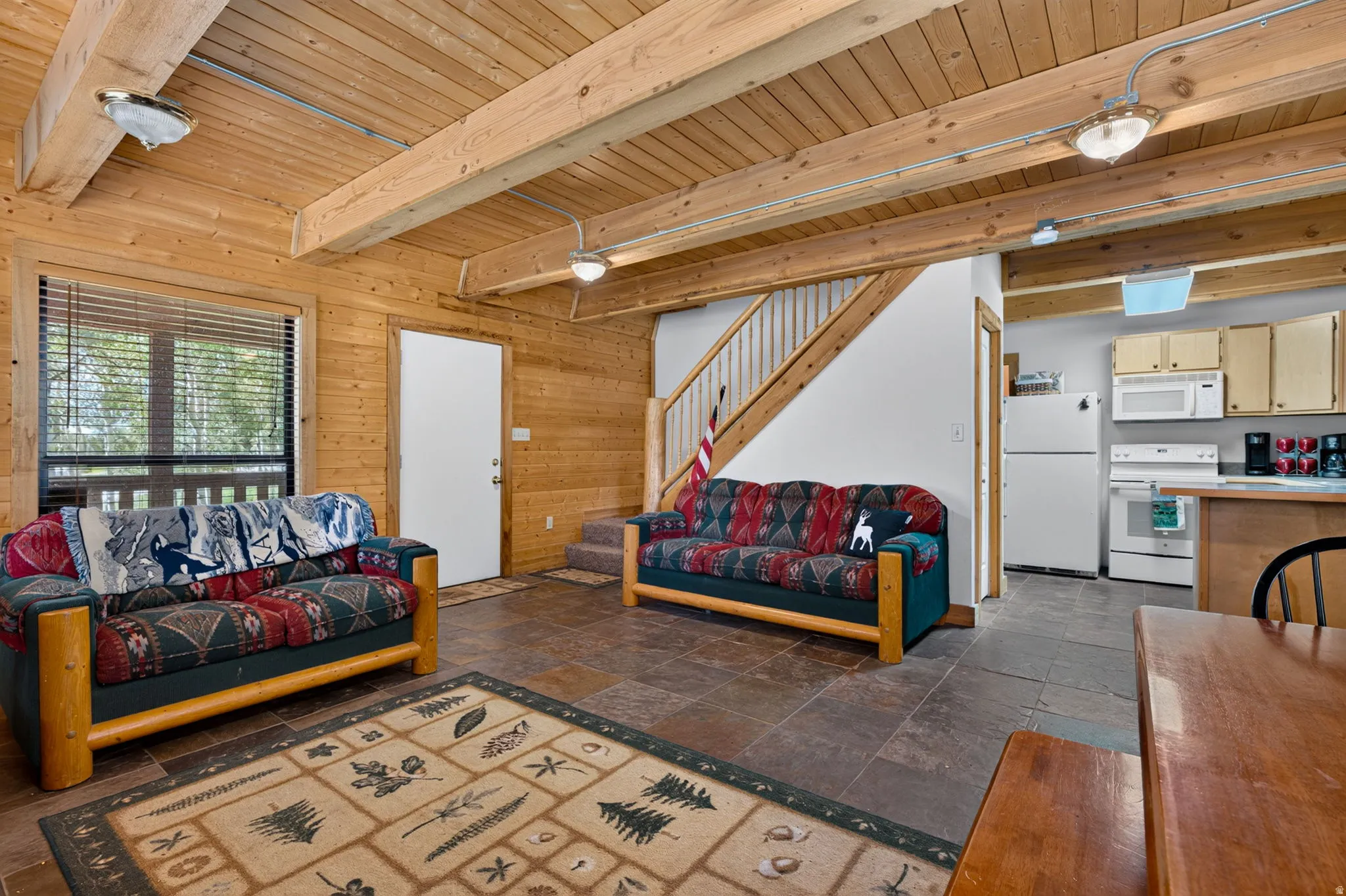 Open-concept living space featuring wood plank walls and ceiling with exposed beams