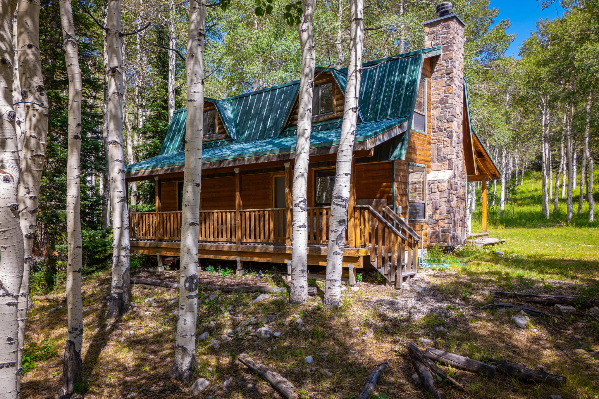 Wood-sided cabin featuring a green metal roof and a stone chimney
