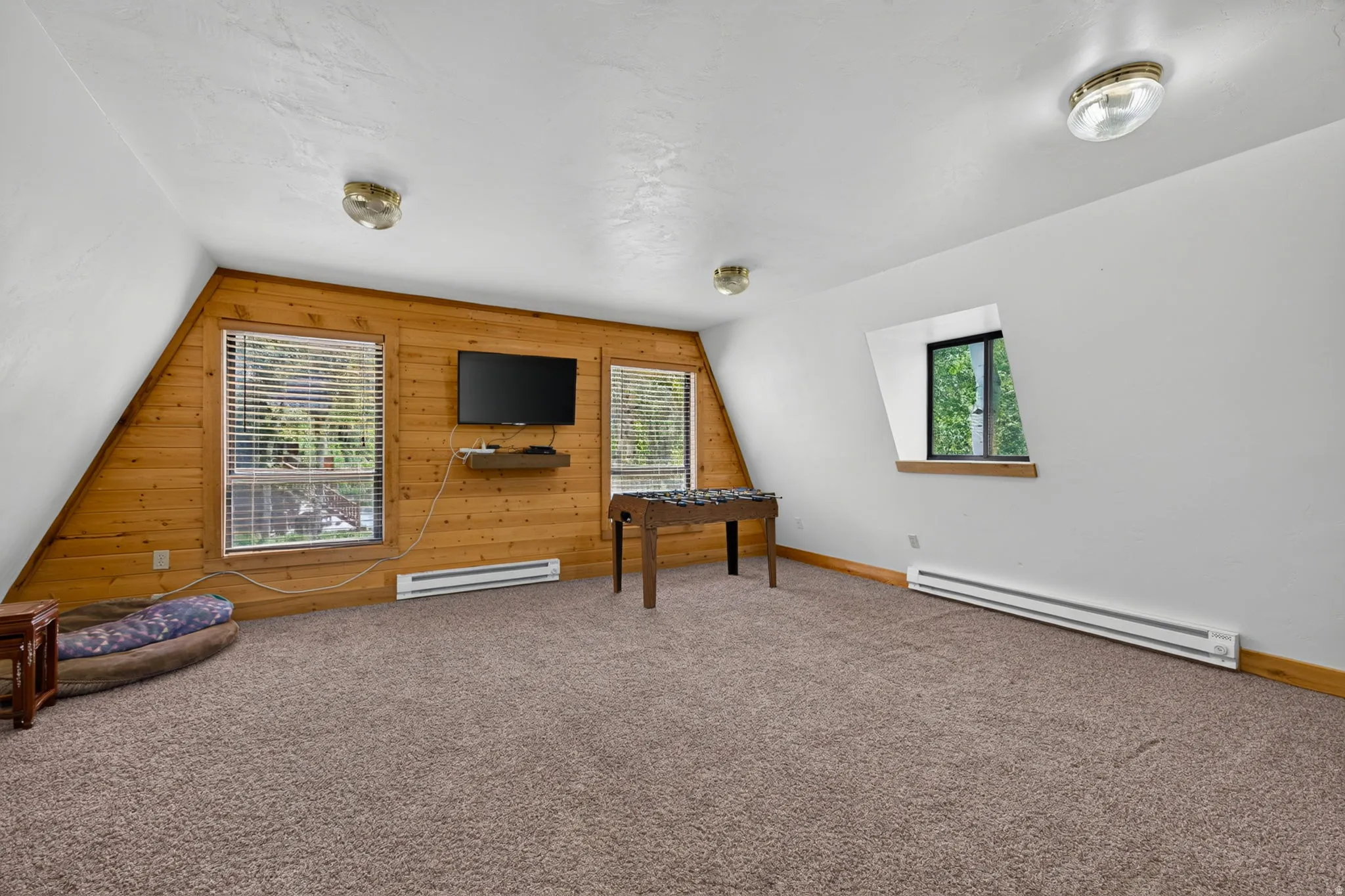 Spacious room featuring sloped ceilings, two large windows with blinds, and a wood-paneled accent wall