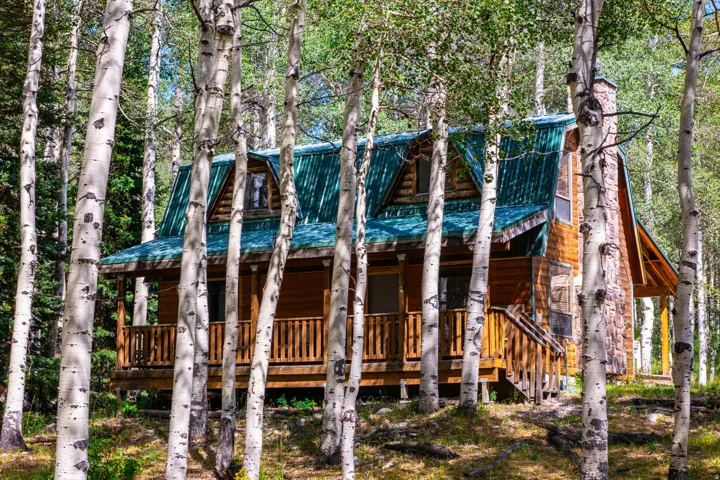 Wood-sided cabin featuring a green metal roof, stone chimney, and covered front porch with wood railings