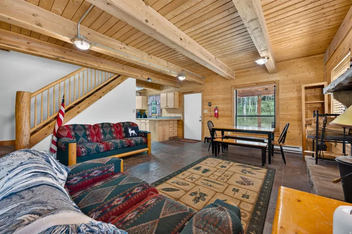 Open-concept living space featuring wood-paneled walls, exposed wood beams, and textured flooring
