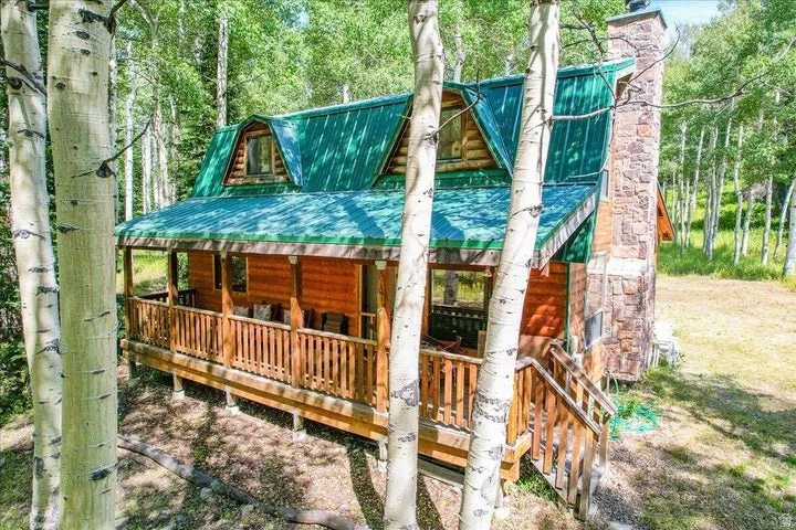 Log cabin exterior featuring a vibrant green metal roof, stone chimney, and an inviting front porch with a wooden railing