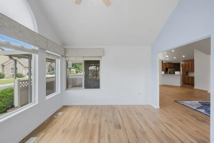 Vaulted ceiling space featuring wood-finish flooring, a ceiling fan, and multiple windows