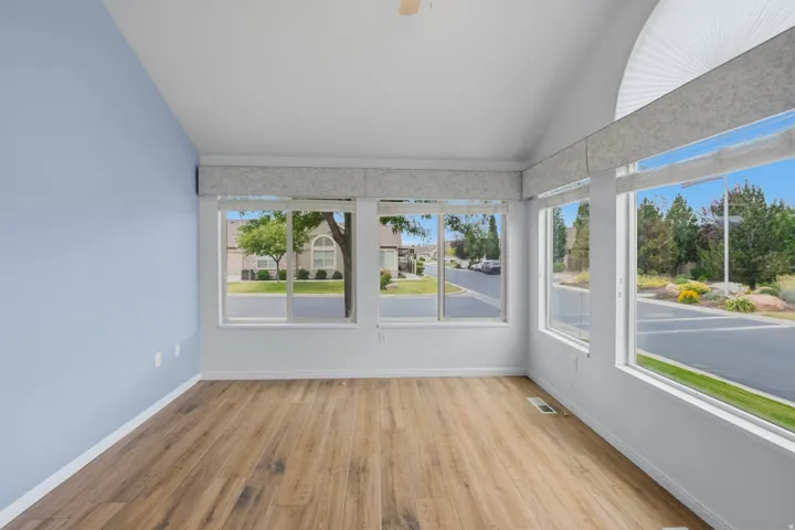 Vaulted ceiling with a ceiling fan, wood-finish flooring, and multiple windows