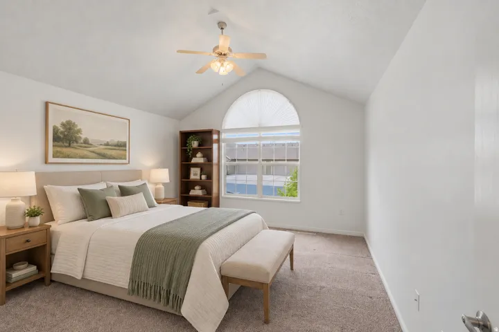 Vaulted ceiling, arched window with blind, ceiling fan, and carpeted flooring