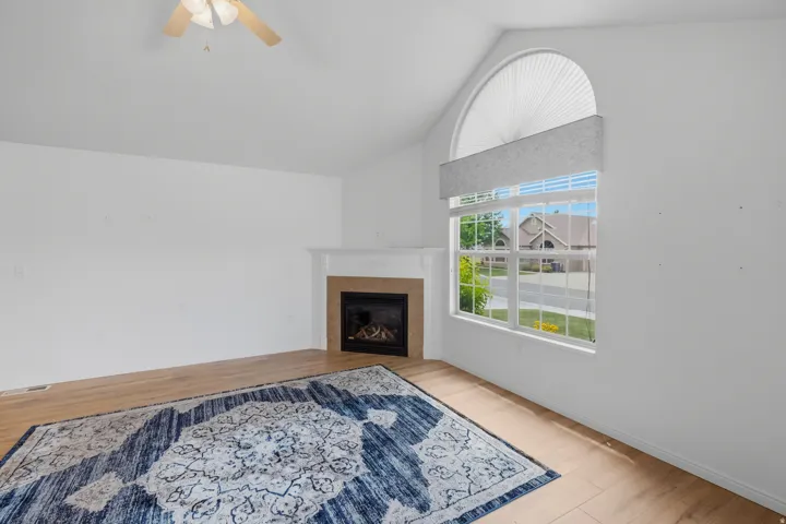 Vaulted ceiling living space featuring a fireplace with a white mantel, a large window with an arched transom, and wood-finish flooring
