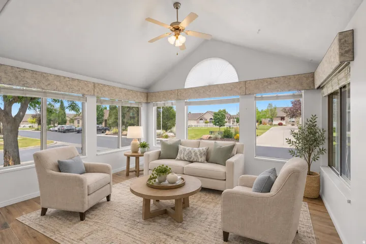 Vaulted ceiling with ceiling fan, wood-finish flooring, numerous windows with custom valances, and an arched transom window