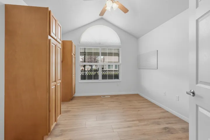 Vaulted ceiling room featuring ample wood-finish cabinetry, a large window with an arched transom, and wood-look flooring