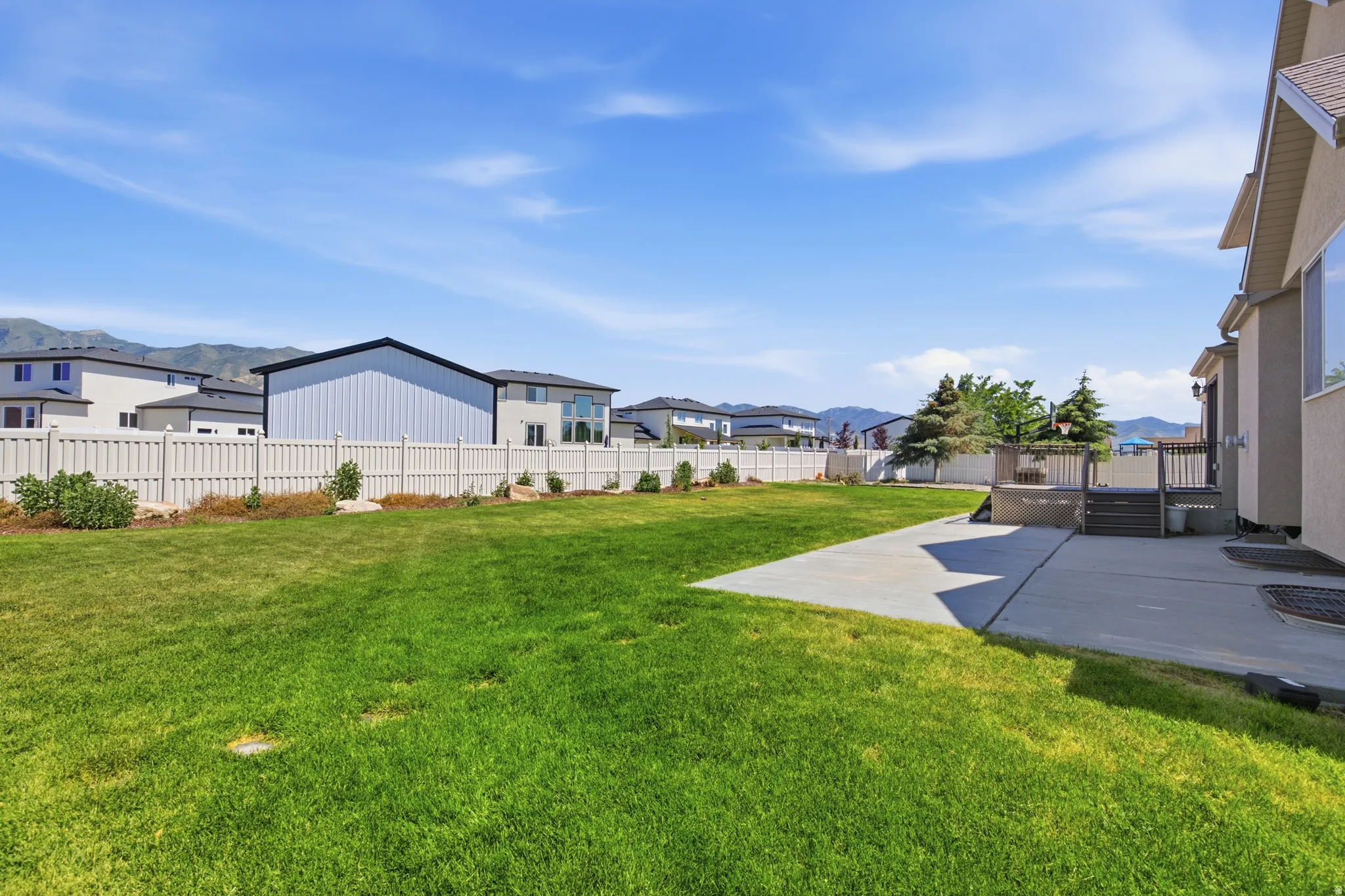 Expansive grass lawn with a concrete patio and a raised wood-finish deck