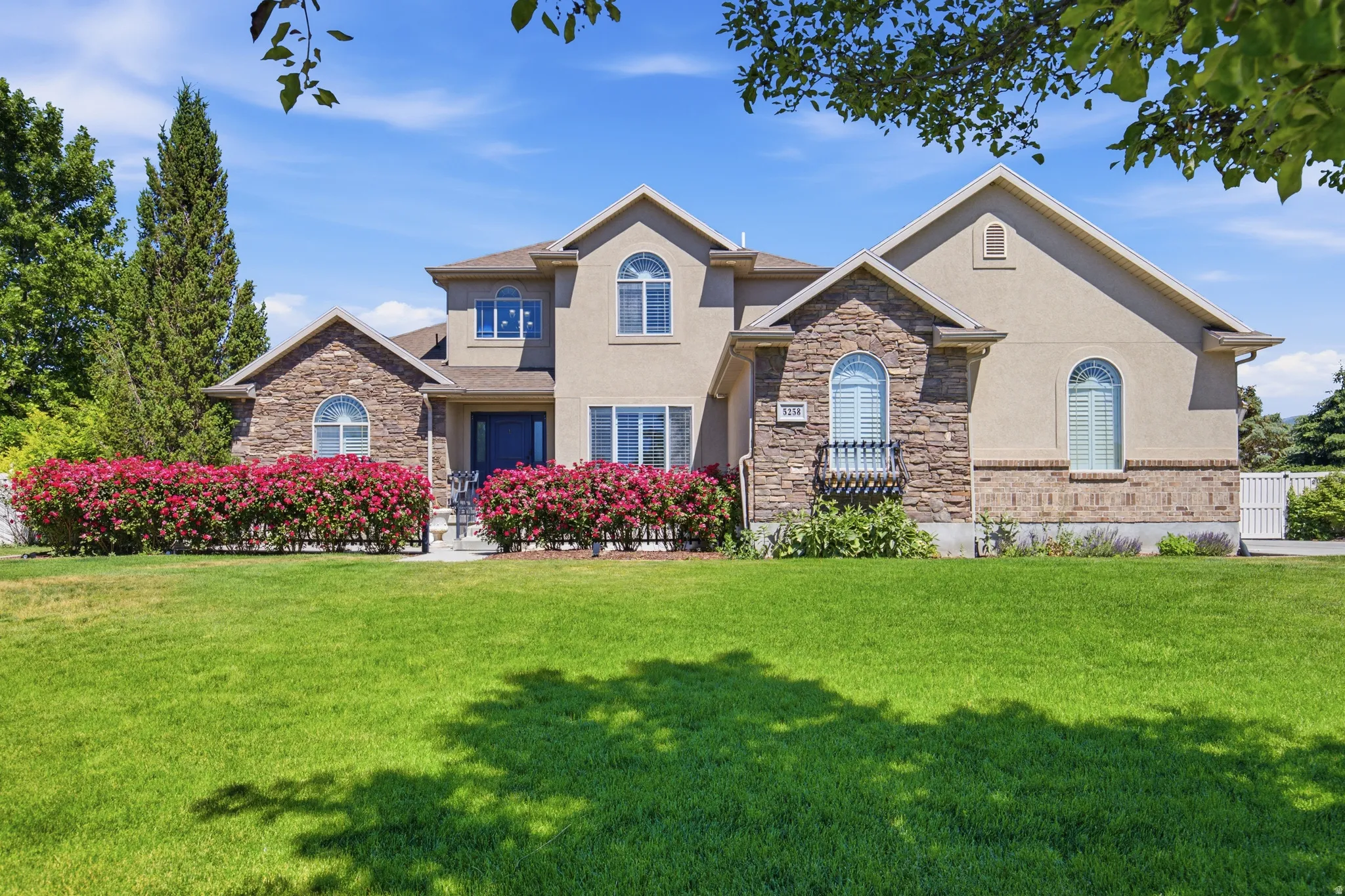 Two-story stucco and stone facade residence featuring arched windows and a prominent front entrance