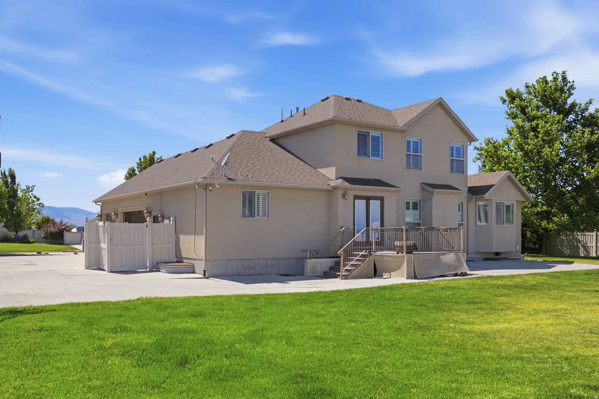 Rear exterior featuring a two-story stucco finish, a private patio with wood railing, a bay window, and a large green lawn