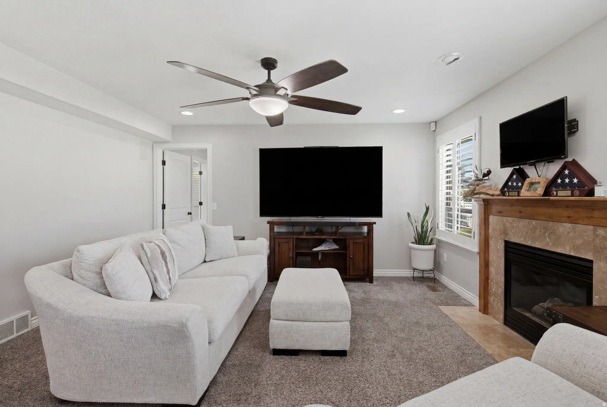 Carpeted living area featuring a ceiling fan, recessed lighting, and a fireplace with a wood-finish mantel and tile surround