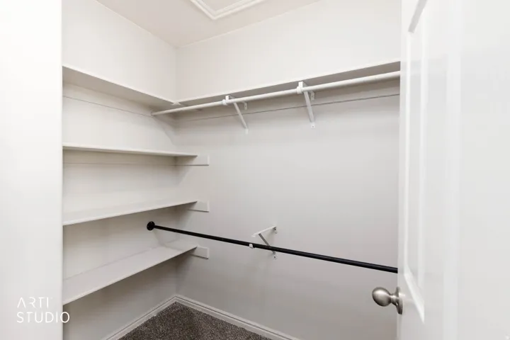 Walk-in closet with multiple white shelving units, two clothing rods, and textured carpeting