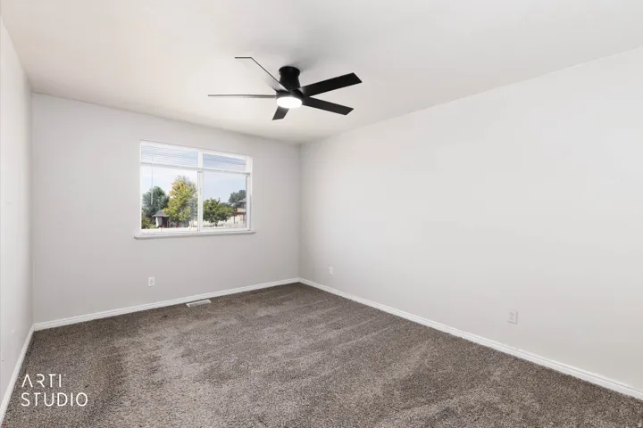 Plush carpeting, neutral wall finishes, window with natural lighting, and a ceiling fan with integrated lighting