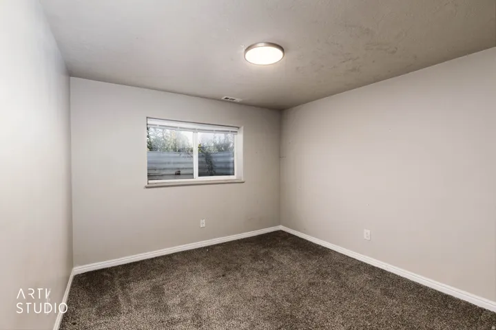 Neutral tone wall paint, flush mount ceiling light, window with white frame, and dark carpet flooring