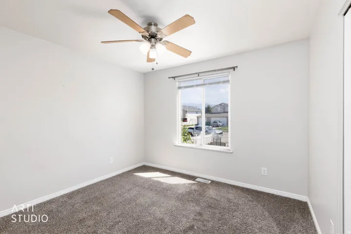 Neutral wall paint, carpet flooring, ceiling fan with integrated lighting, and a single window