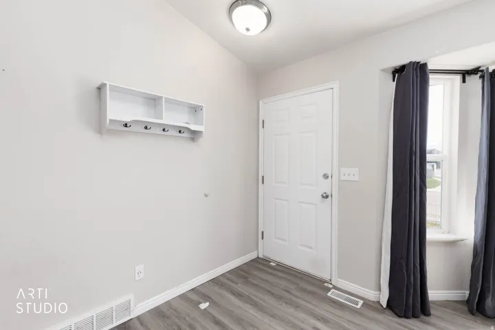 White paneled door, wood-finish flooring, and a wall-mounted shelving unit with hooks