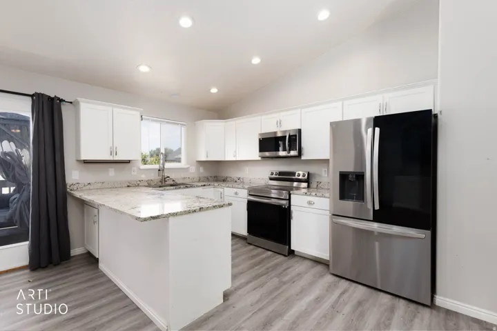 White cabinetry, light-toned countertops, stainless steel appliances, wood-finish flooring, and recessed lighting