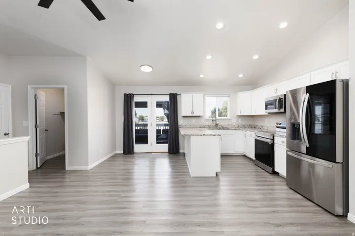 Open-concept living area featuring wood-finish flooring, white cabinetry, stainless steel appliances, and a kitchen island with stone countertops