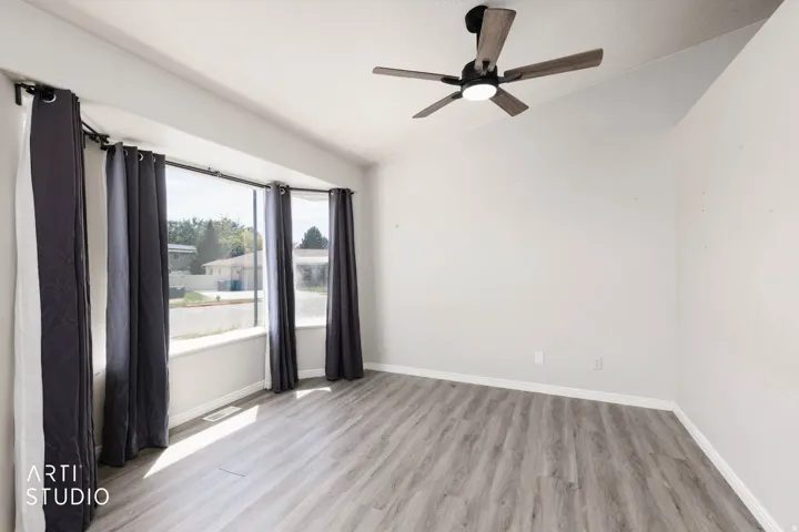 Angled ceiling featuring a modern ceiling fan, bay window, light gray walls, and wood-finish flooring