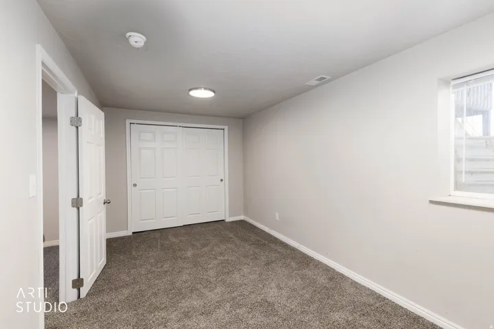 Neutral wall finish, gray carpet flooring, white trim, window with blinds, and white bi-fold closet doors
