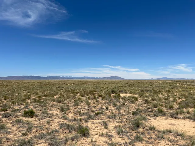 Expansive open terrain with sparse natural vegetation, featuring distant mountain ranges and a clear blue sky
