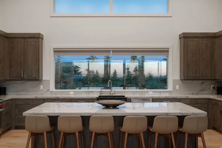 Spacious kitchen featuring an expansive central island with seating, extensive wood cabinetry, marble-finish countertops, and a large picture window