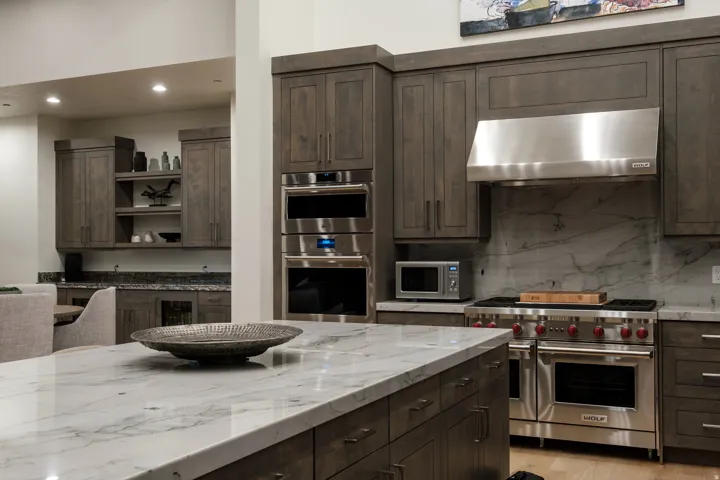 Gourmet kitchen featuring a large island with a substantial stone countertop, custom wood cabinetry, stainless steel professional-grade appliances, and a full-height stone slab backsplash